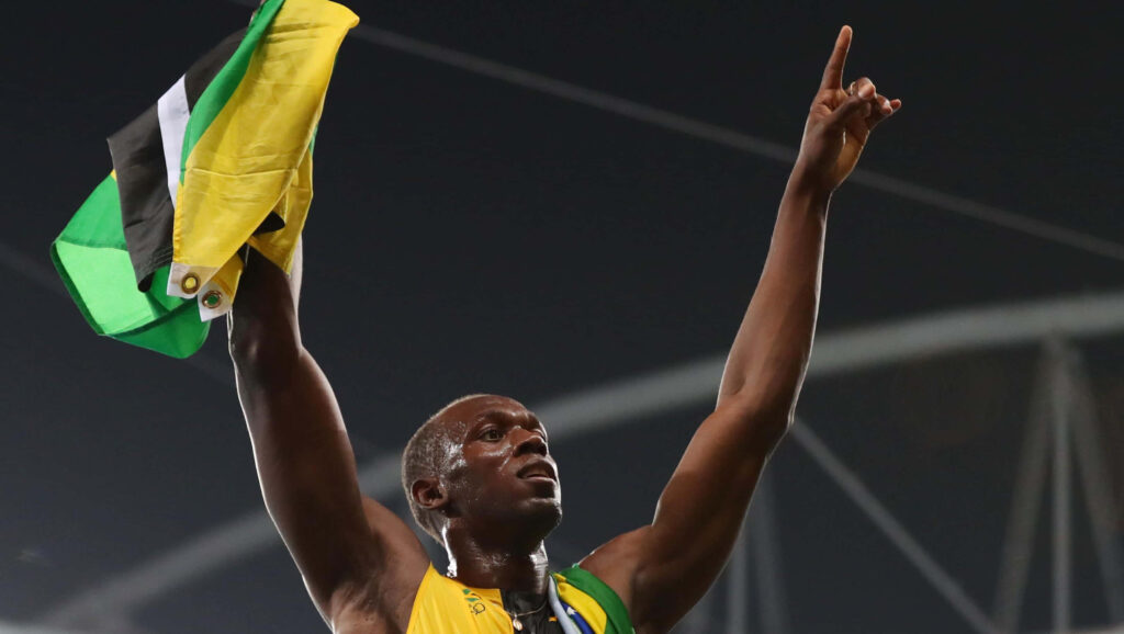 Usain Bolt triumphantly holds Jamaican flag celebrating victory in stadium inspirational wallpaper