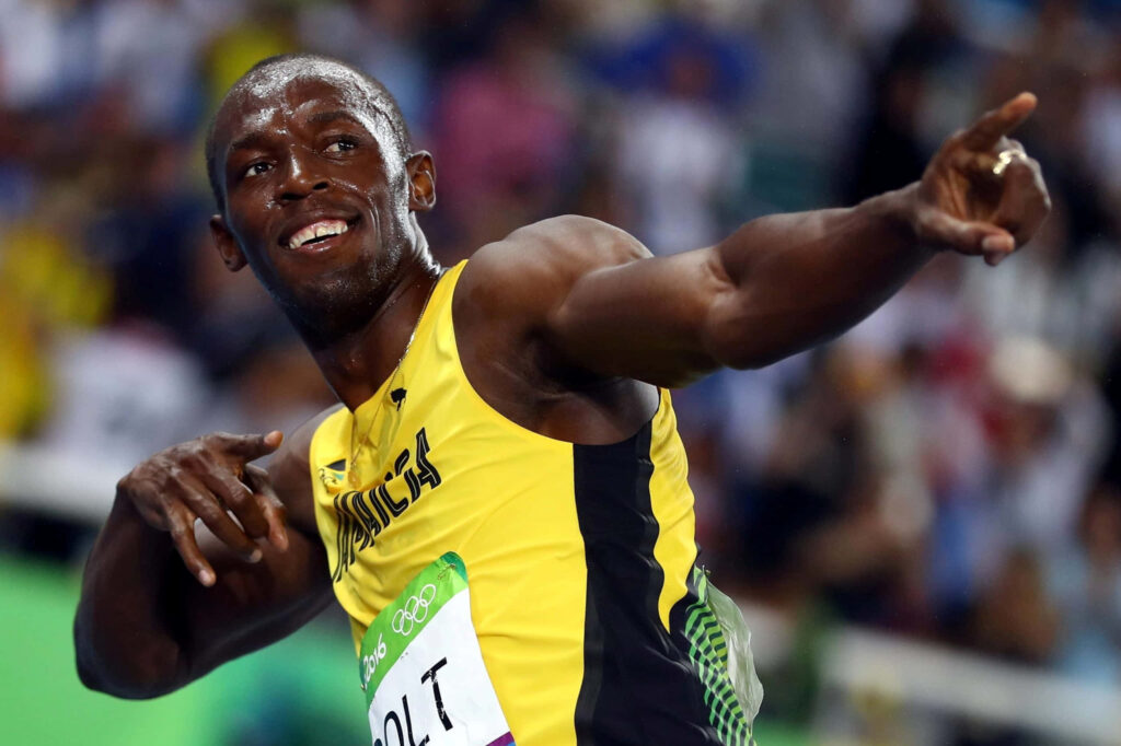 Usain Bolt smiling and pointing right in Jamaican track uniform iconic celebration wallpaper