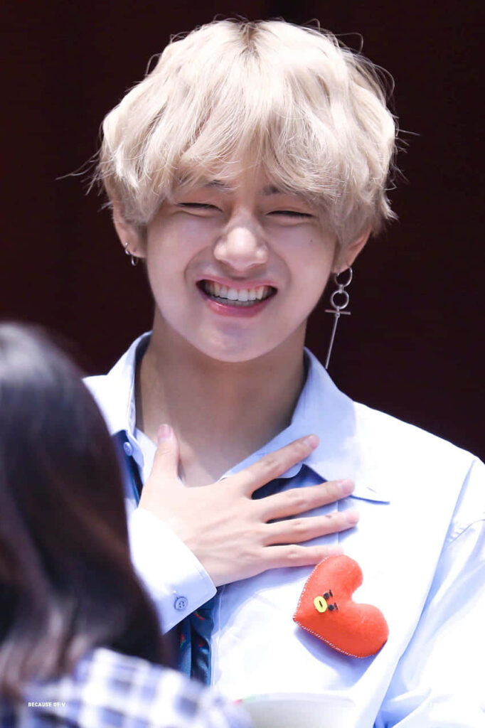 V from BTS smiling brightly creating a joyful cheerful phone wallpaper background image