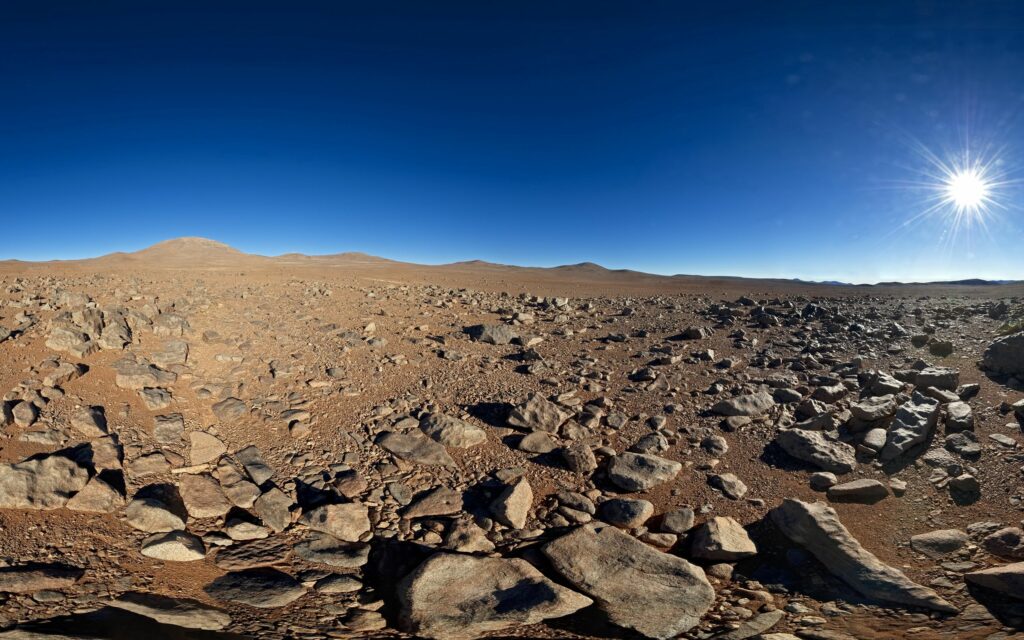 Vast desert landscape with rugged stones coarse sand under clear blue sky and bright sun Wallpaper