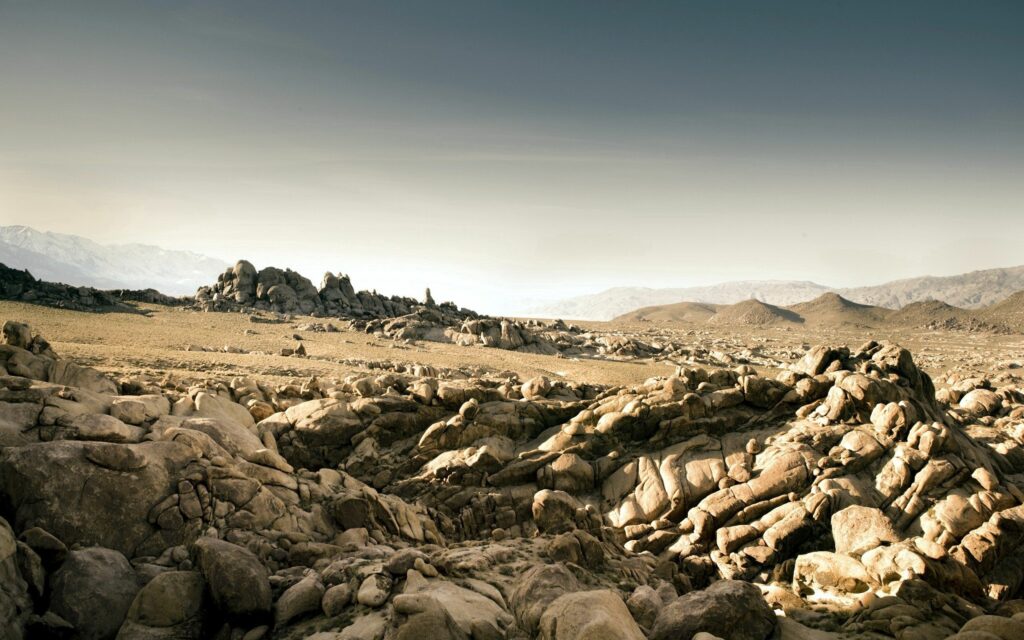 Vast desert landscape with rugged stones sandy terrain and hazy sky earthy tones wallpaper background