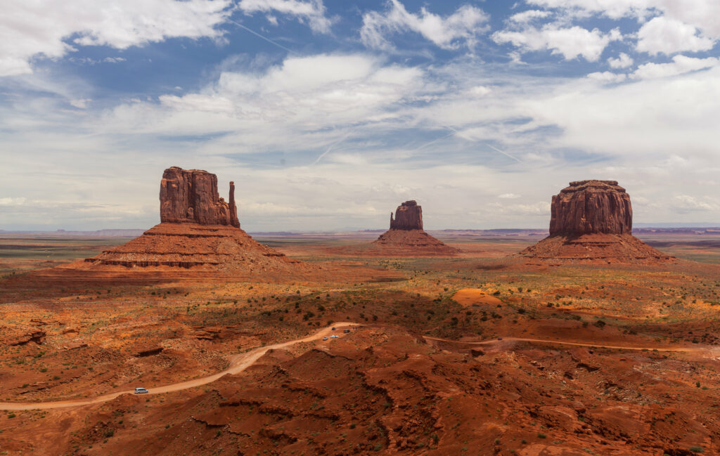Vast desert landscape with winding road red rock buttes open prairie bright blue sky clouds wallpaper