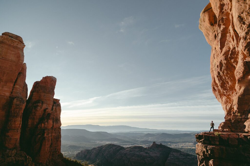 Vast canyon with red cliffs jagged rocks lone silhouette on edge under clear sky wallpaper background