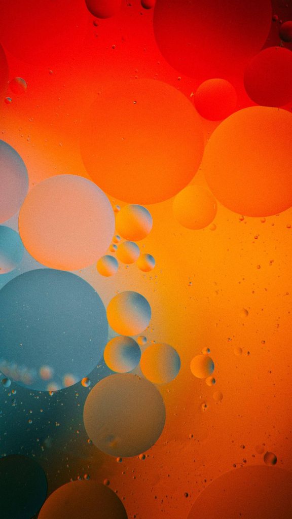 Abstract macro photography of vibrant orange red and blue bubbles floating in fluid background Wallpaper