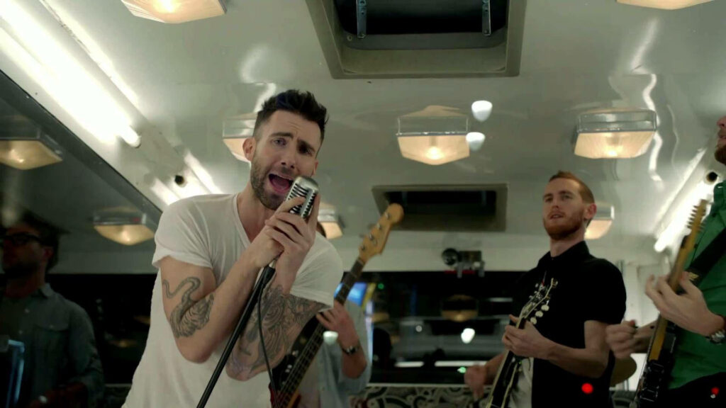 Adam Levine passionately performing with Maroon 5 in vibrant indoor wallpaper backdrop.