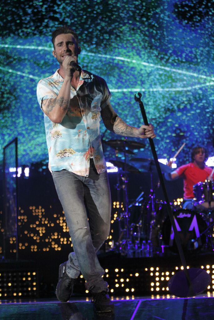 Adam Levine performing on stage in vibrant casual attire with dynamic lighting and tattoos. Wallpaper