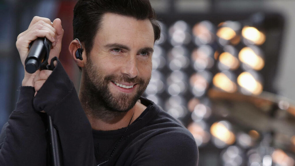 Vibrant Adam Levine wallpaper, smiling with microphone against a warm, dreamy background.
