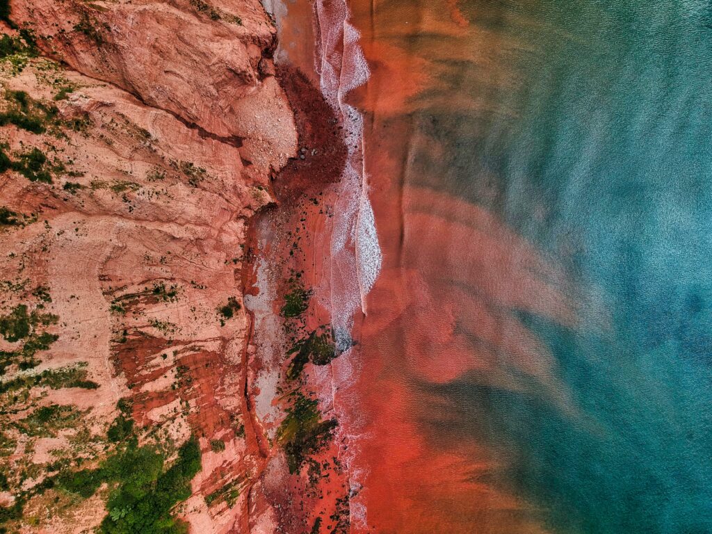 Aerial view of vibrant red canyon rocks meeting blue water with foamy surf shoreline wallpaper