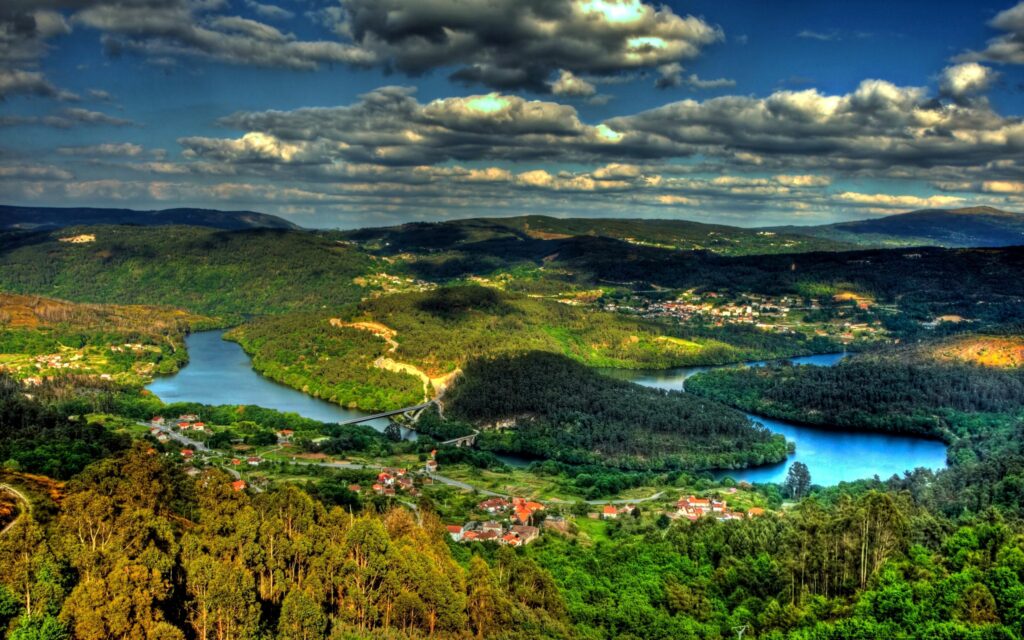 Aerial view of island with winding rivers lush forests rolling hills and distant cityscape under dramatic clouds Wallpaper