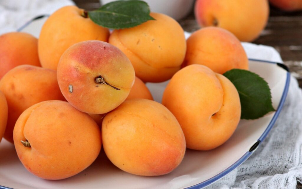 Vibrant Apricot Wallpaper: Fresh Orange Fruit with Greenery Background