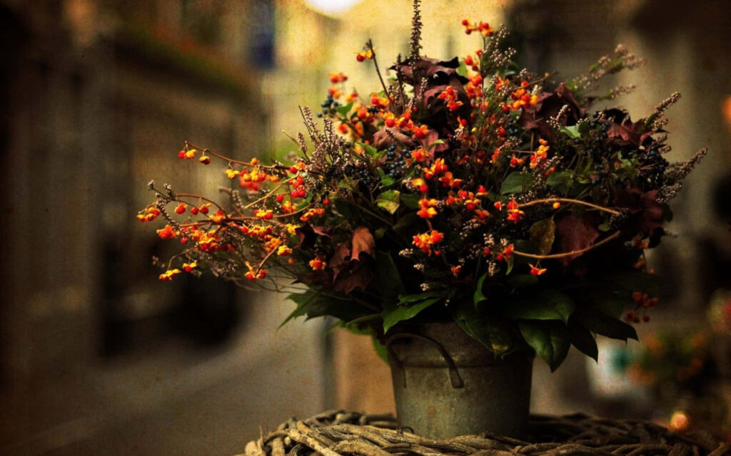 Rustic Metal Flower Pot with Vibrant Autumn Flowers on Woven Mat Wallpaper