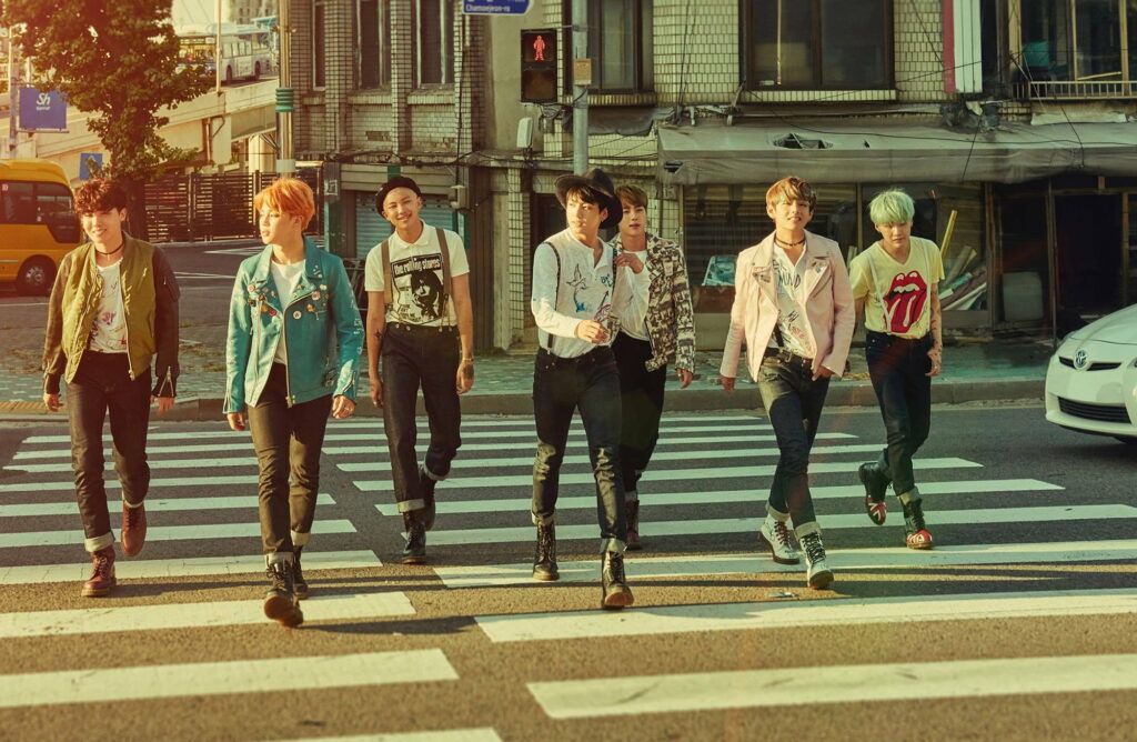 BTS members walking on urban crosswalk in stylish street fashion under warm golden sunlight Wallpaper