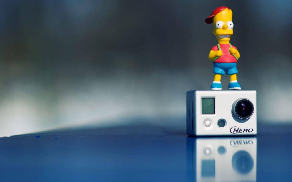 Vibrant Bart Simpson figurine on white GoPro Hero camera with reflective blue tech background Wallpaper