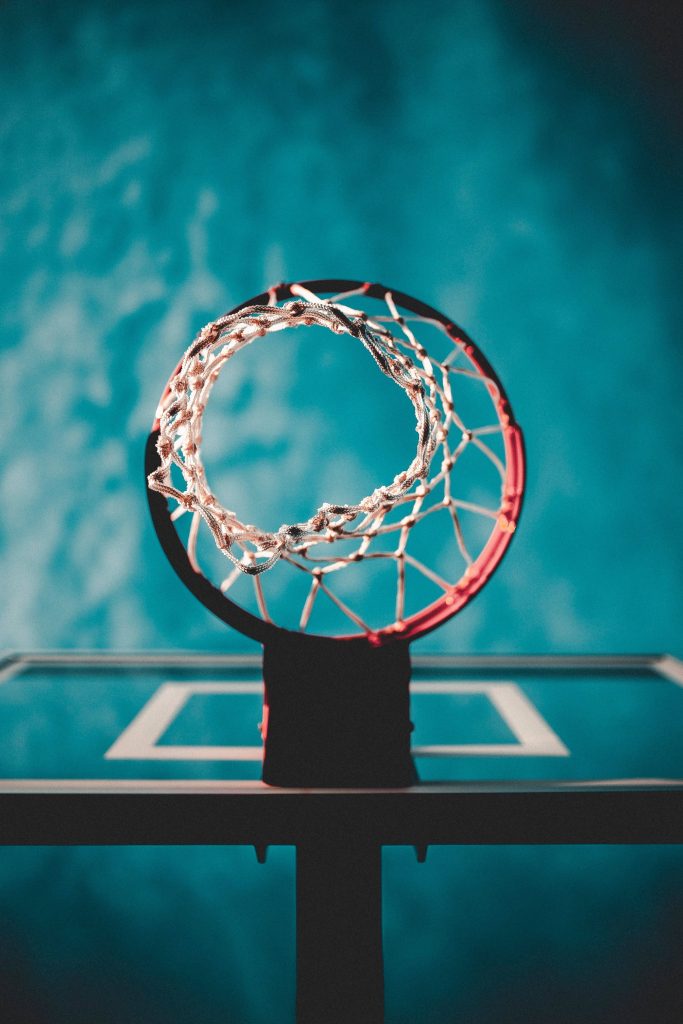 Low angle vibrant orange basketball hoop and net with turquoise sky basketball wallpaper background