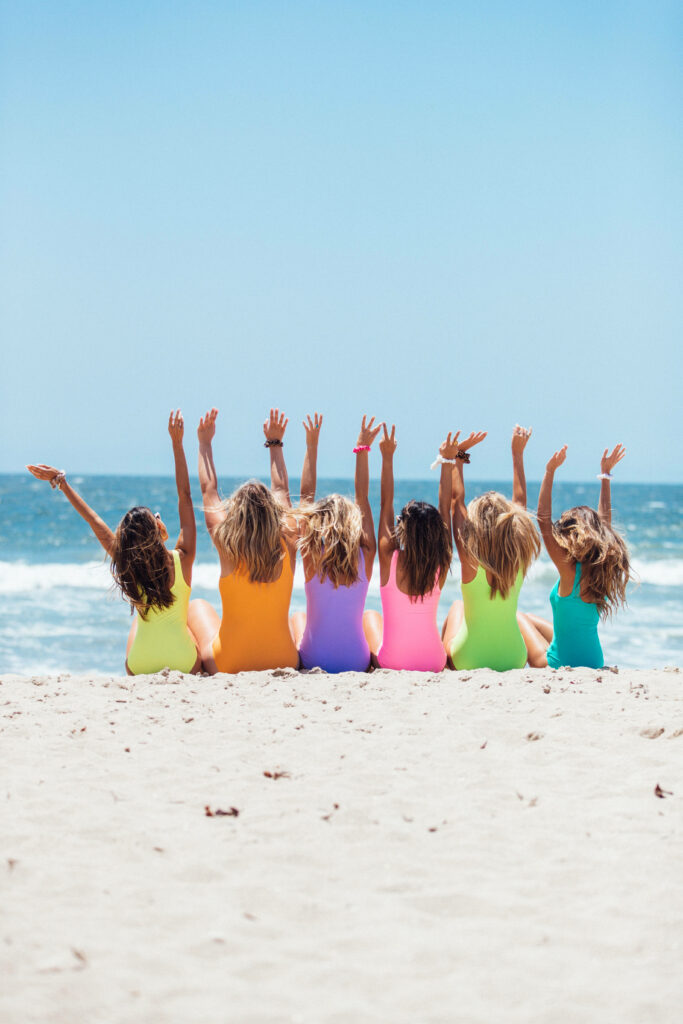 Joyful Beach Scene: Friends in Colorful Swimsuits Against Blue Sky Wallpaper
