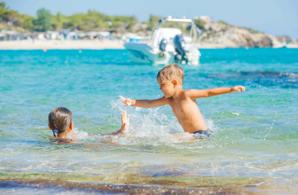 Joyful Beach Day: Child Splashing in Crystal-Clear Waters Wallpaper