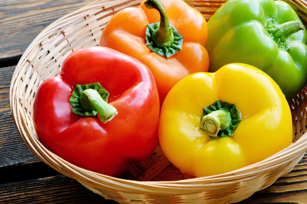 Vibrant wallpaper of fresh red yellow orange and green bell peppers in rattan basket background