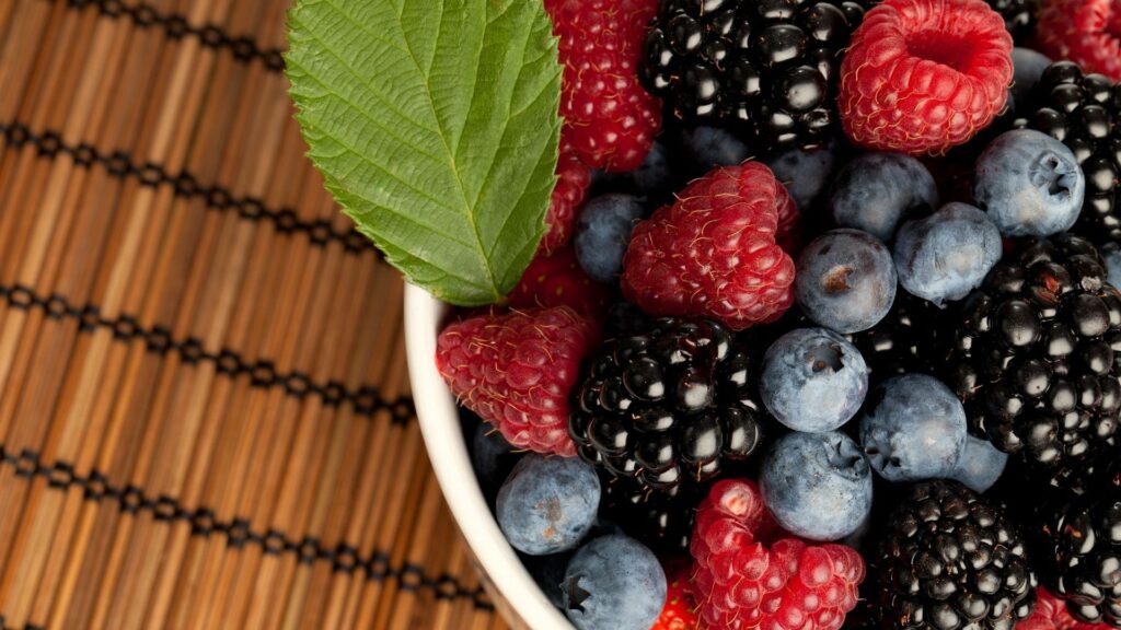 Vibrant Berry Plate Wallpaper with Wooden Texture and Green Leaf