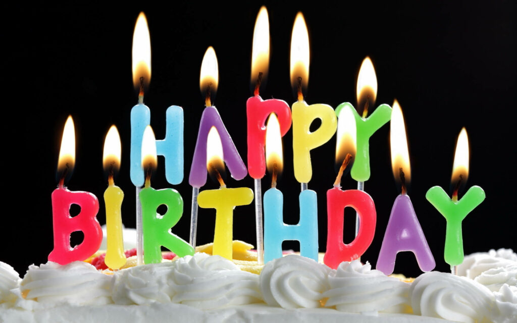Vibrant birthday cake wallpaper with colorful candles glowing warmly on festive icing swirls