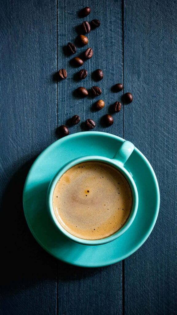 Steaming black coffee in turquoise cup with coffee beans on dark wooden background wallpaper