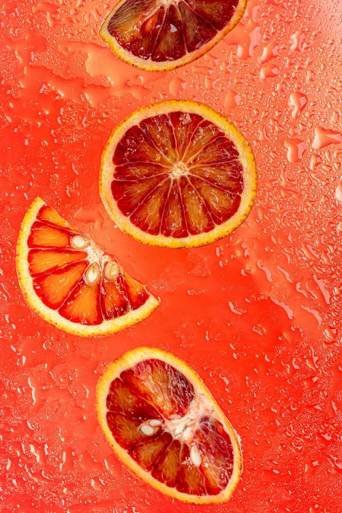 Vibrant blood orange slices on red textured surface with glistening water droplets wallpaper