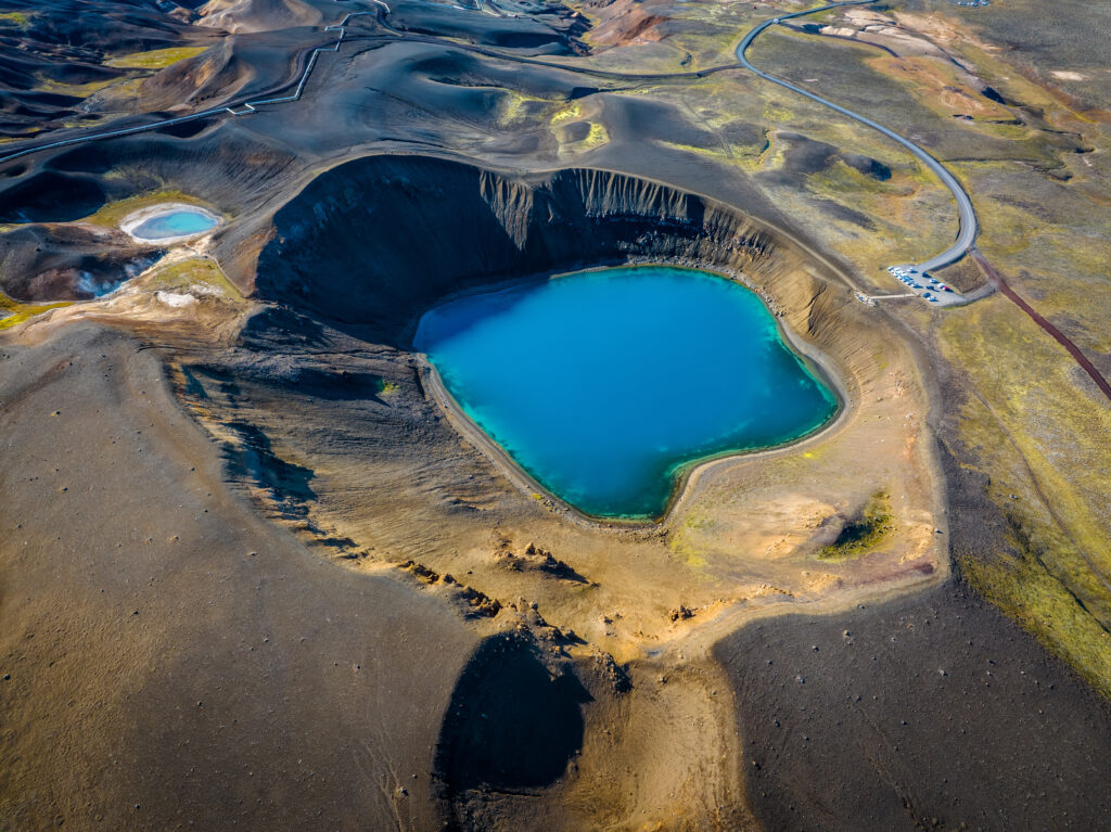Vibrant blue crater lake in rugged volcanic landscape with earthy tones and sparse vegetation wallpaper