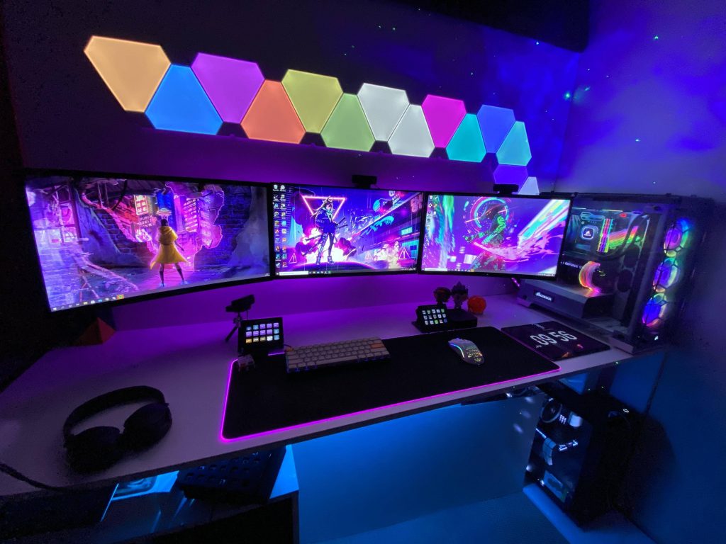 Vibrant blue cyberpunk gamer room wallpaper with triple RGB monitors and Nanoleaf panels