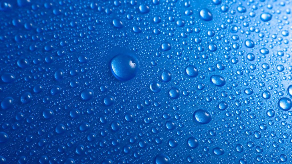 Macro view of clear water droplets on vibrant blue background with bright light reflections Wallpaper