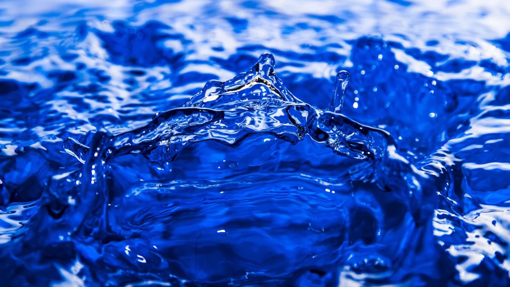 High-speed macro of vibrant blue water splash with white highlights on deep azure background Wallpaper