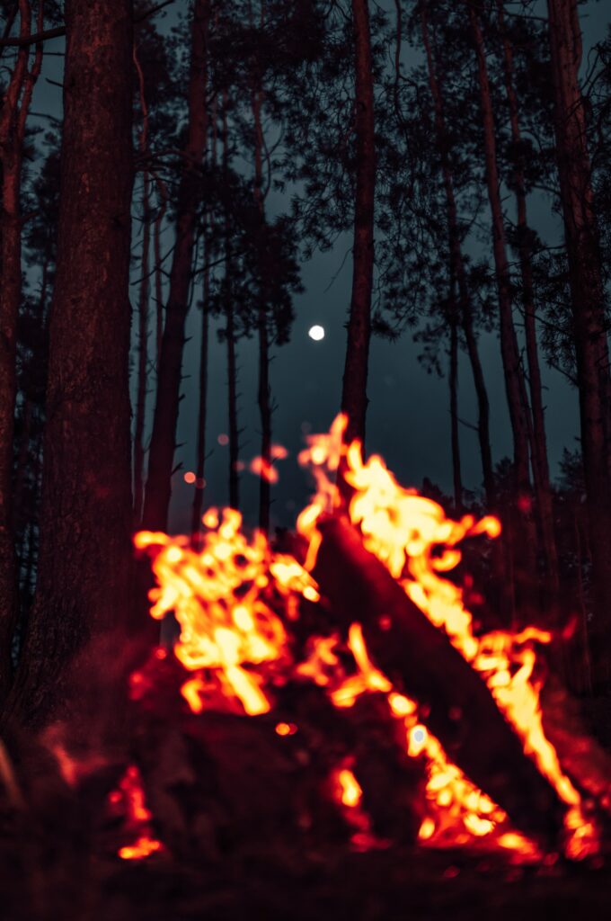 Vibrant bonfire glowing with sparks in dark forest under full moon silhouette nighttime scene wallpaper
