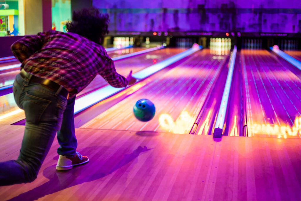 Focused player rolling blue bowling ball on polished wooden lane vibrant neon bowling alley wallpaper