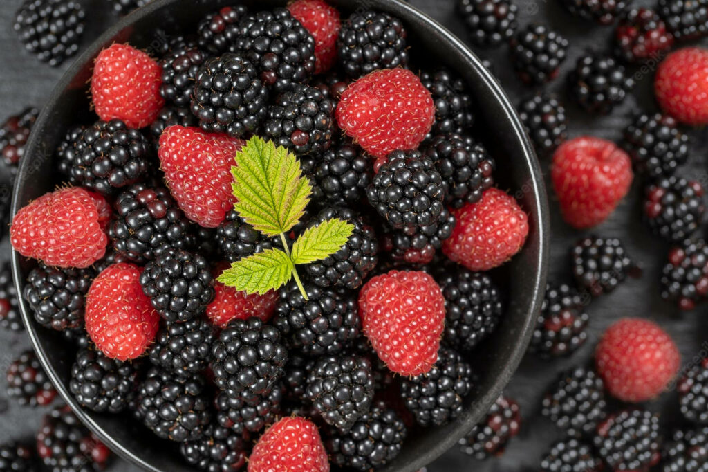 Close-up of ripe glossy boysenberries with green leaves vibrant healthy fruit wallpaper background