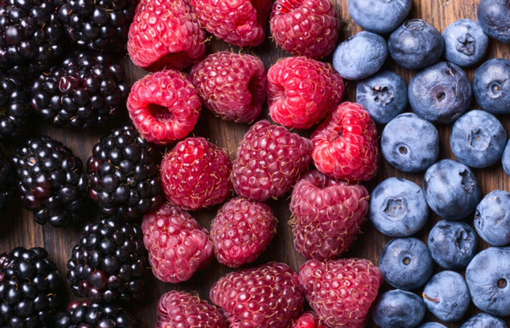Colorful boysenberries raspberries and blueberries arranged on rustic wooden surface closeup Wallpaper