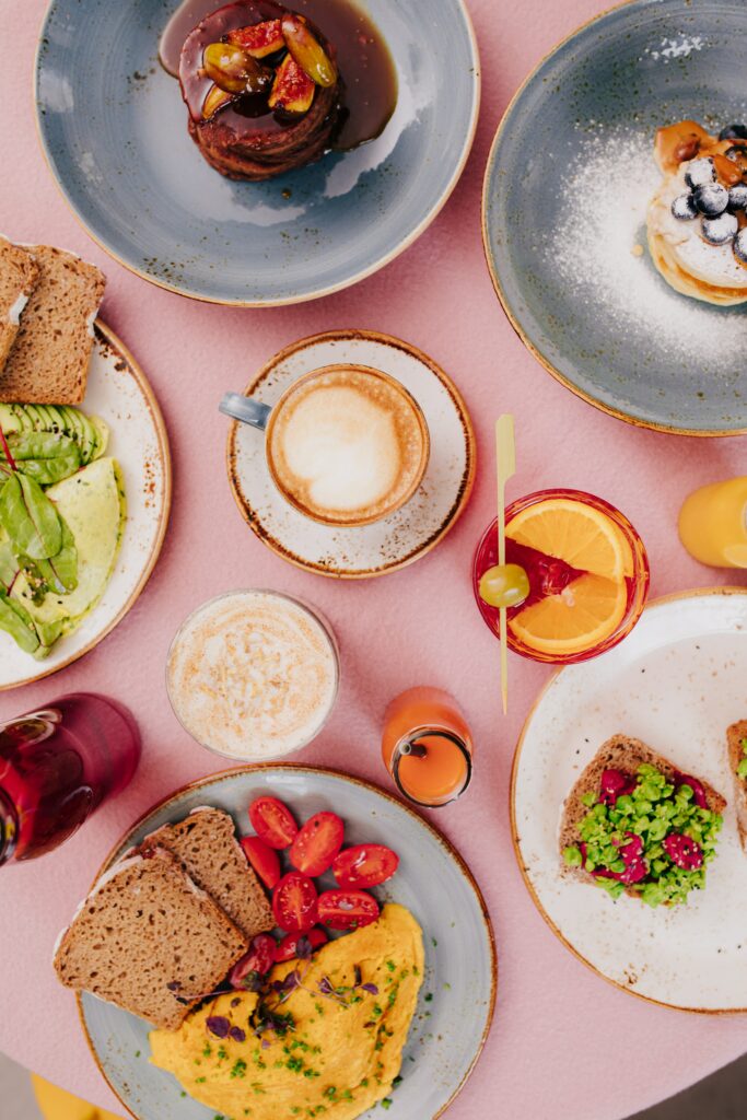 Colorful Breakfast Spread: Avocado Toast, Omelet & Pancakes on Pink Wallpaper