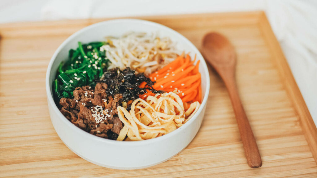 Colorful Bulgogi Bibimbap bowl with marinated beef vegetables seaweed and sesame seeds on tray Wallpaper