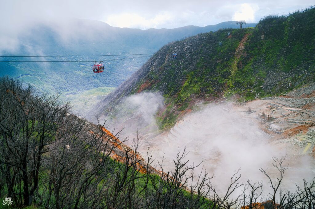 Vibrant cable car gliding above misty hills and rugged mountains in foggy natural landscape Wallpaper