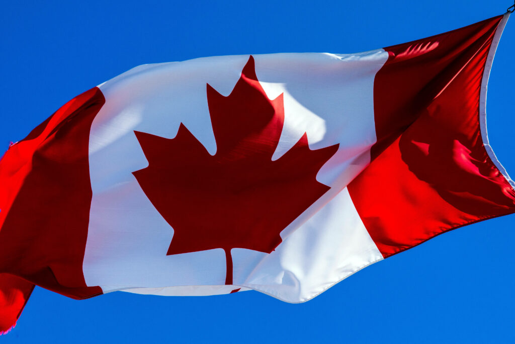 Close-up of Canadian flag with vibrant red maple leaf and bold colors against blue sky background Wallpaper