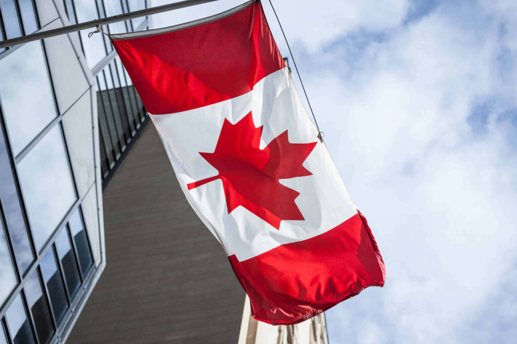 Canadian flag waving beside modern building with glass windows under partly cloudy sky wallpaper