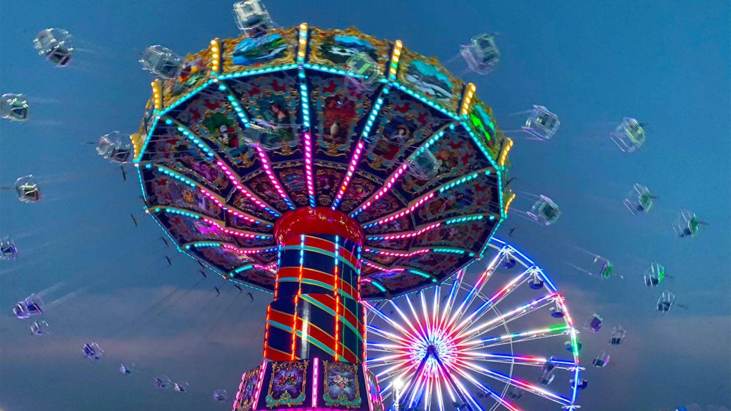 Vibrant carnival wallpaper with illuminated swing ride and glowing Ferris wheel at twilight
