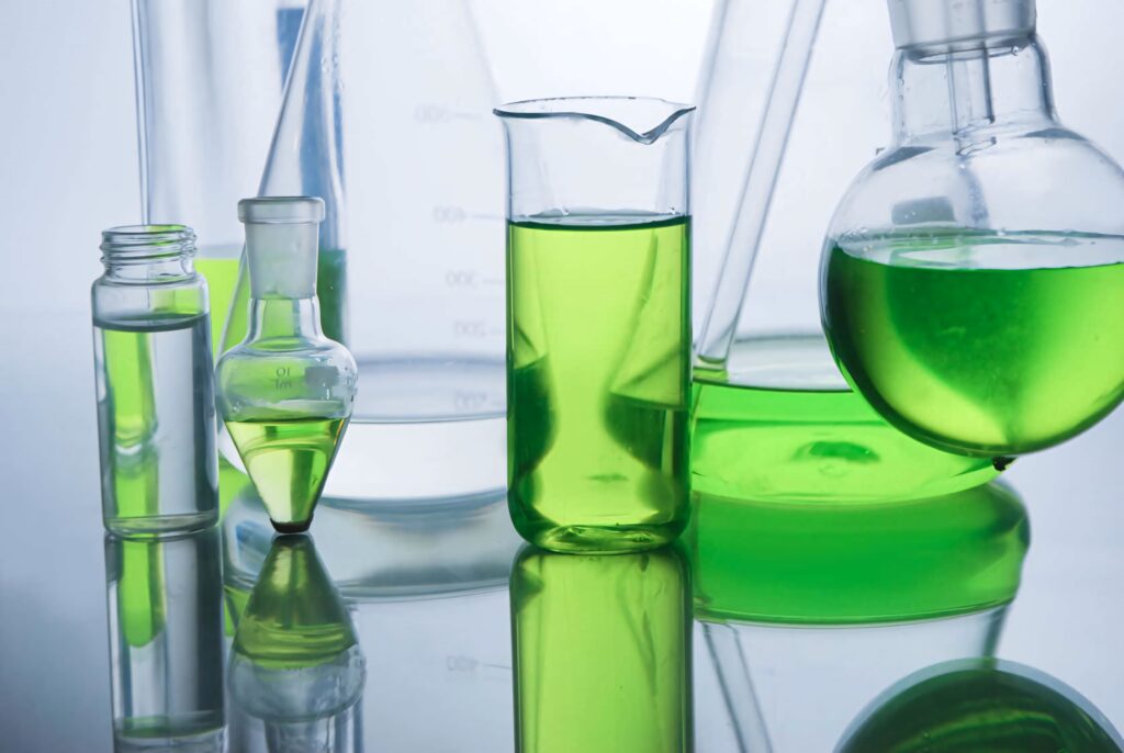 Vibrant chemistry lab with green liquid in glass beakers and flasks on reflective surface background Wallpaper