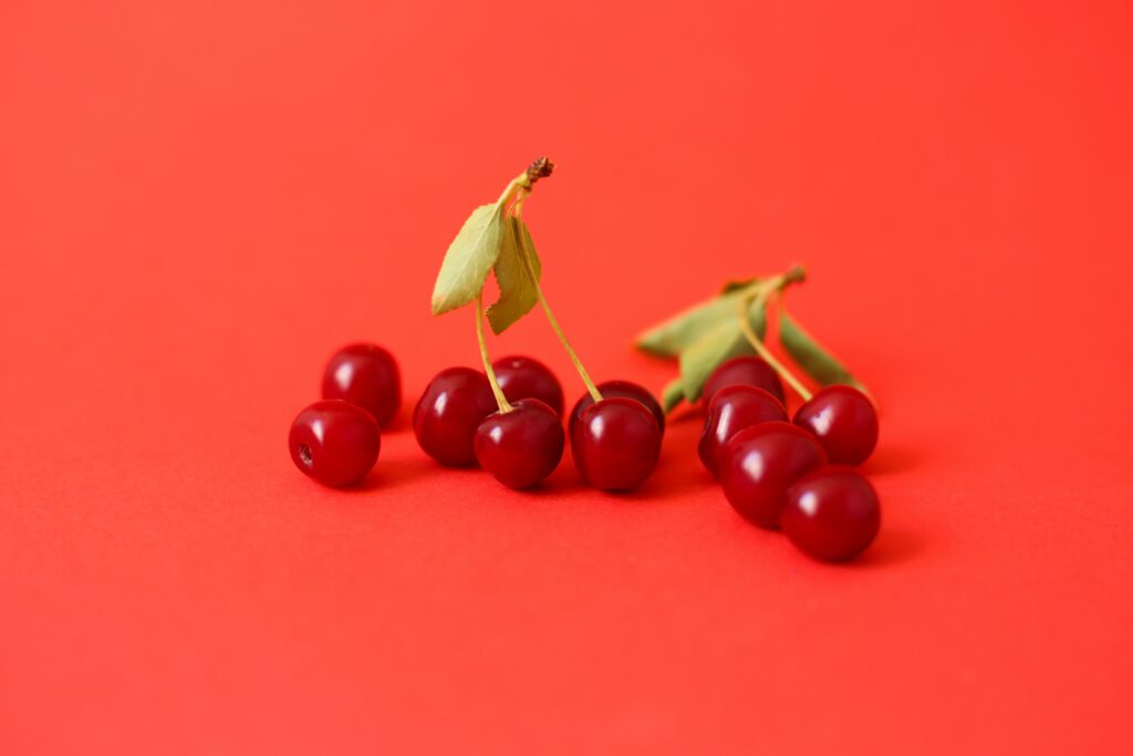 Vibrant Red Cherry Wallpaper: Lush Green Leaves on Bold Background