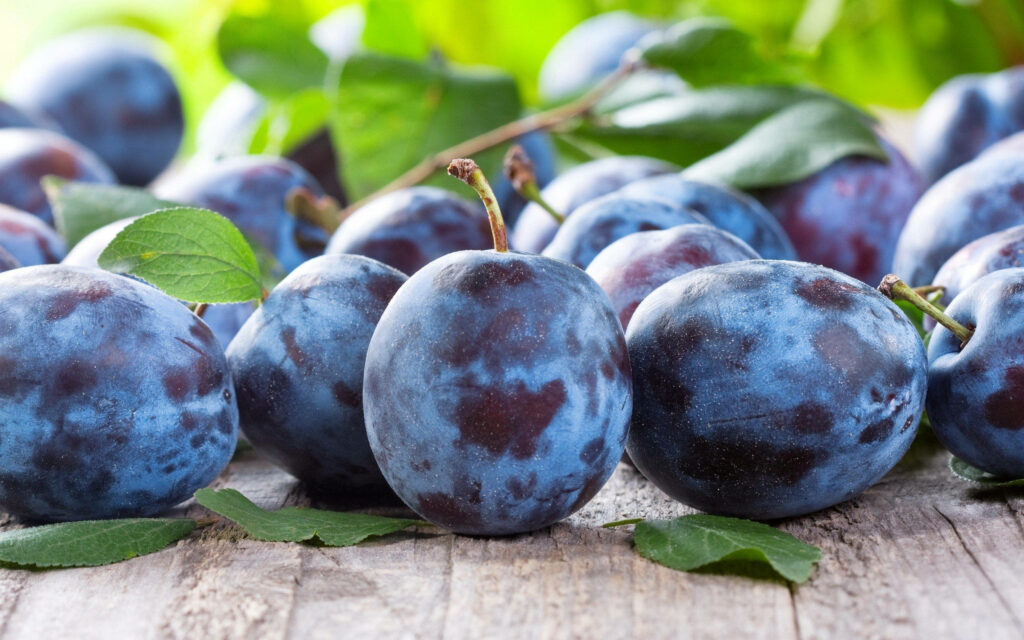 Vibrant Chilean Plum Varieties Wallpaper on Rustic Wooden Surface