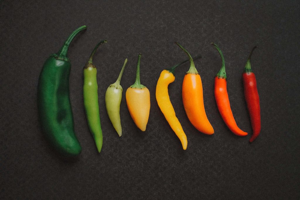 Colorful flat-lay of eight fresh chili peppers arranged in a green to red spectrum on dark background Wallpaper