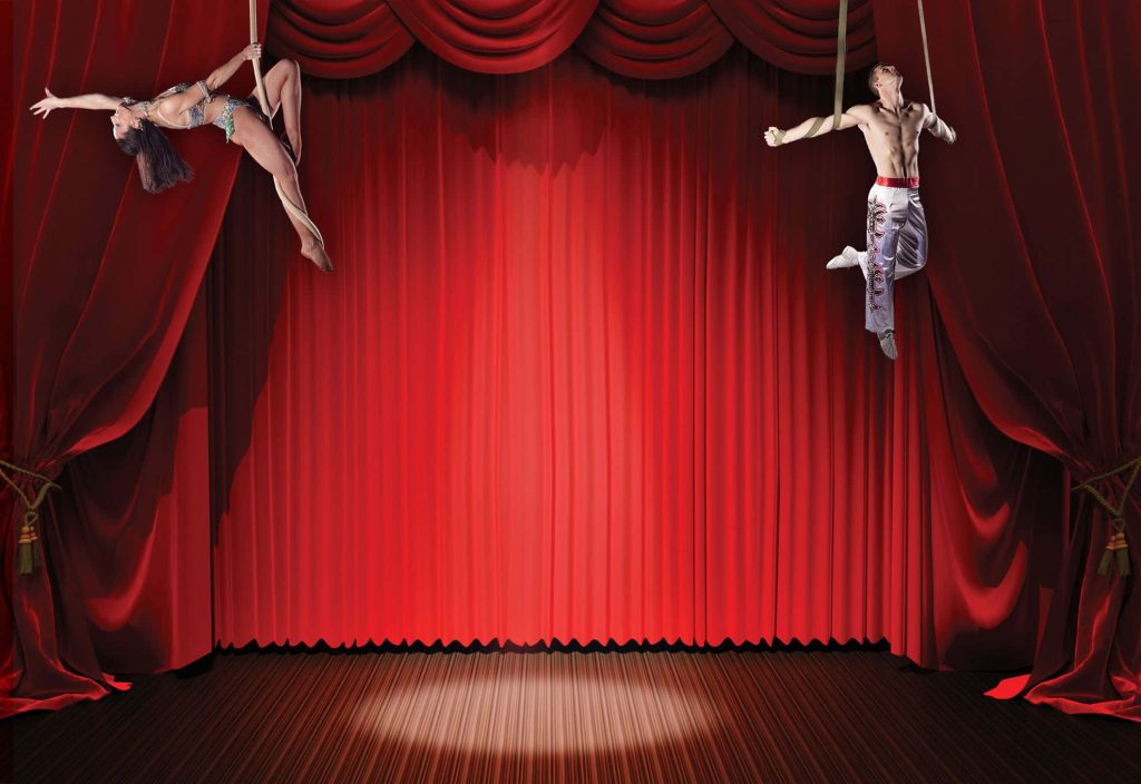 Two aerial acrobats perform under spotlight on red velvet curtains circus wallpaper background