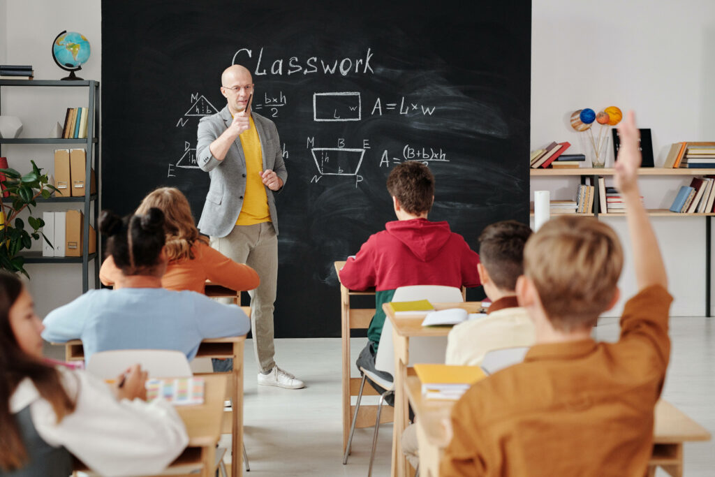 Teacher explains math formulas to engaged students in vibrant classroom with chalkboard and globe Wallpaper