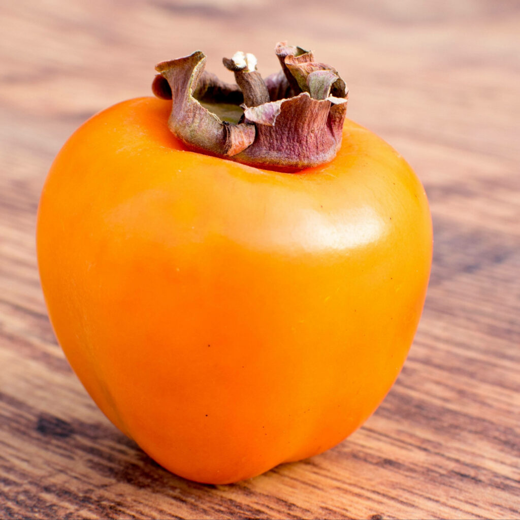 Vibrant Close-Up of Ripe Persimmon on Wooden Surface - Wallpaper