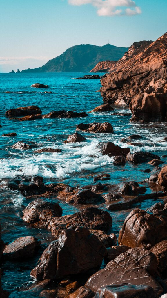 Vibrant coastal wallpaper with rugged brown mountains and turquoise waves crashing on rocky shores