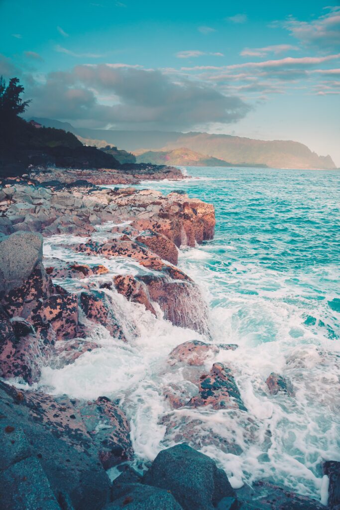 Vibrant coastal landscape with rugged rocks and crashing ocean waves under blue sky wallpaper
