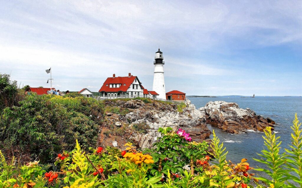 Vibrant coastal landscape with white lighthouse red roof rocky cliffs colorful flowers blue sea Wallpaper