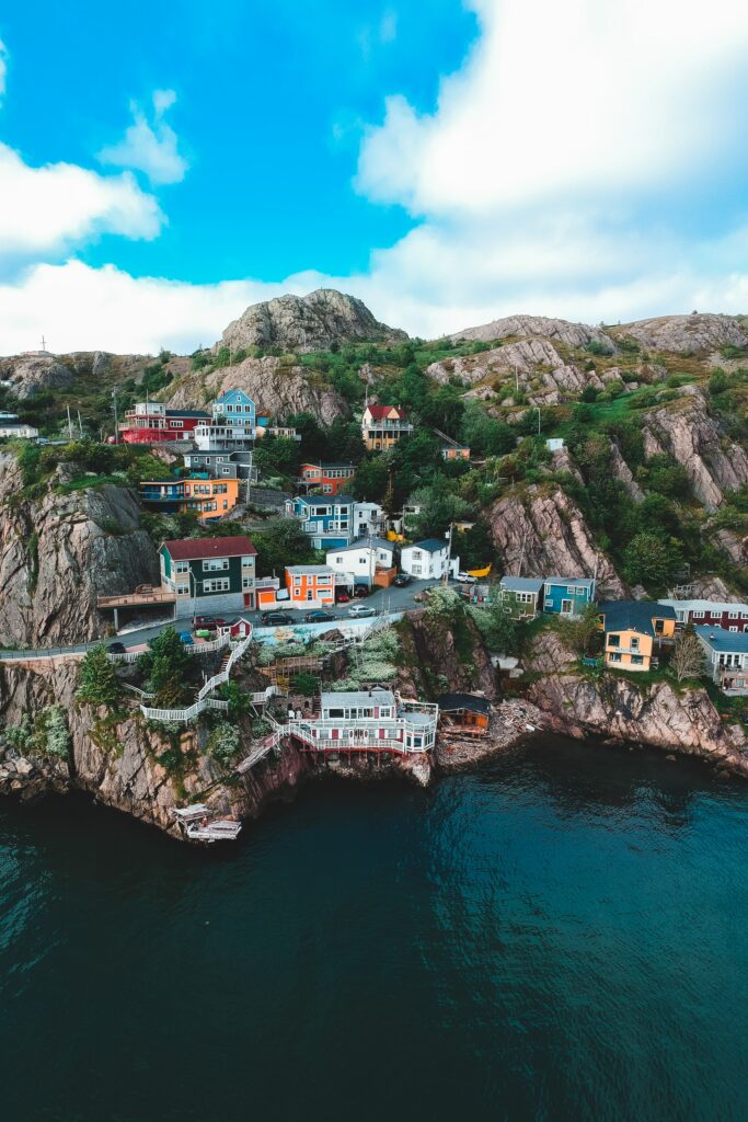 Colorful coastal town buildings on cliffs with blue sea mountains and lush greenery background Wallpaper